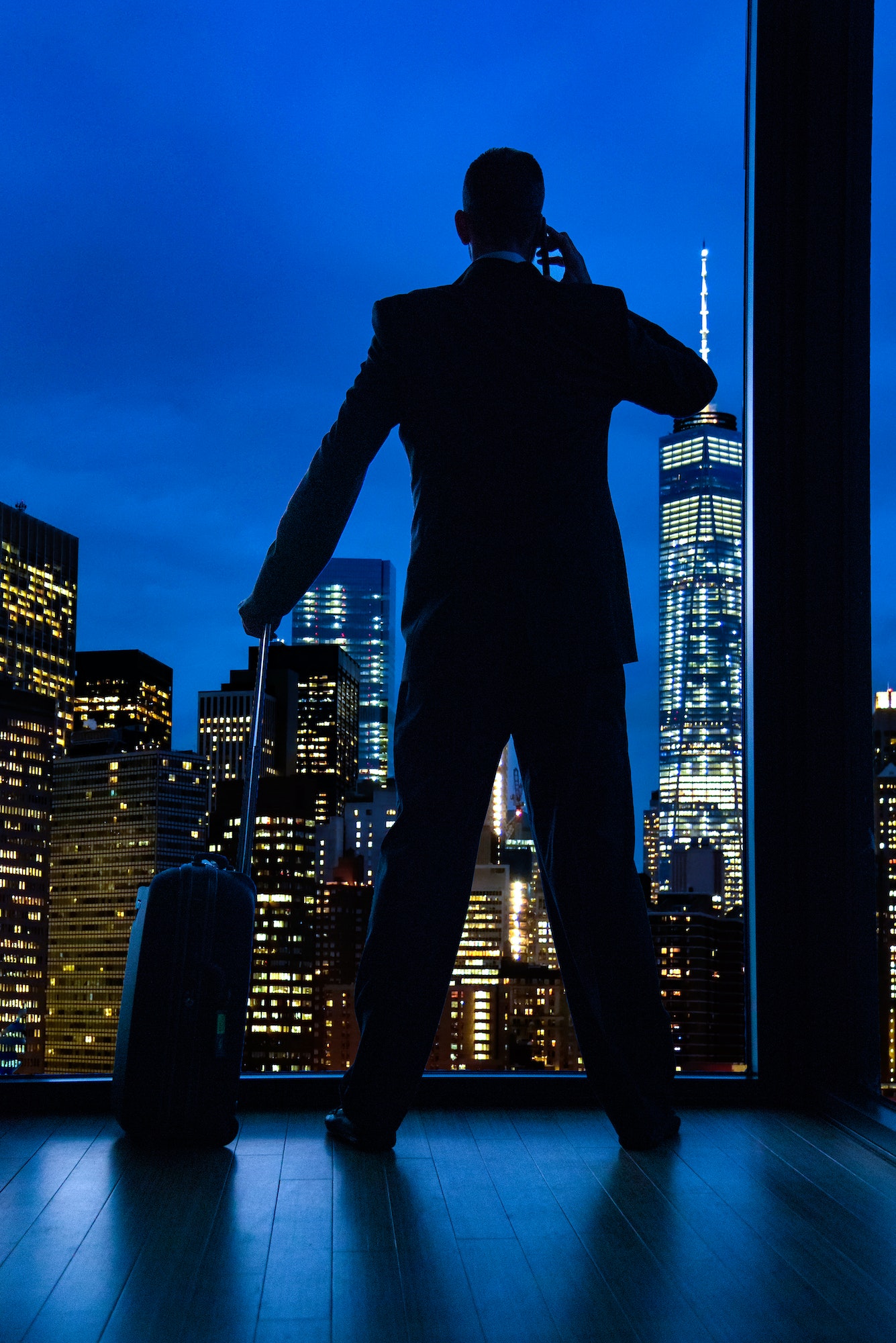 Silhouette traveller at night on phone with luggage.